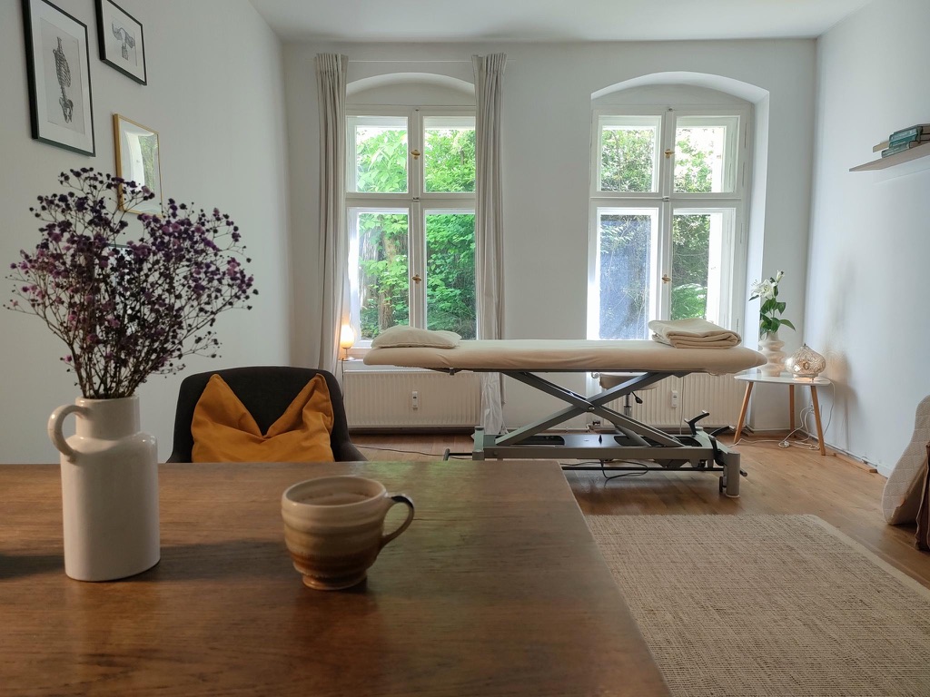 Studio space with two large windows, a massage table and a desk